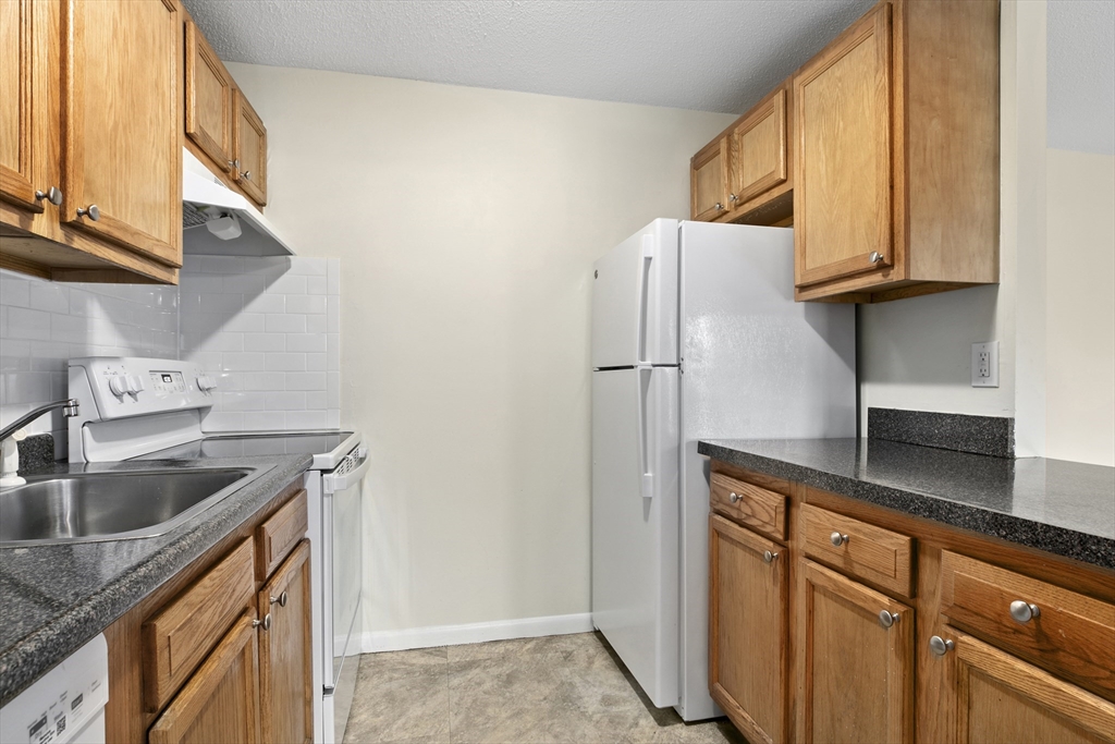 68 Main Street, Unit 17C Stoneham, MA 02180 - Photo 5 of 13 a kitchen with granite countertop a sink a refrigerator and cabinets
