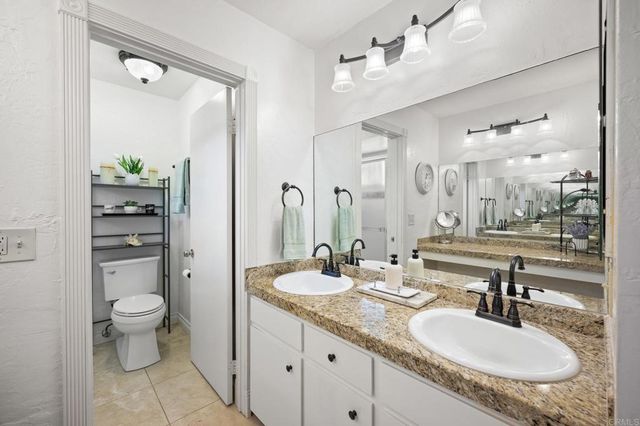 a bathroom with a granite countertop double vanity sink a mirror and a toilet