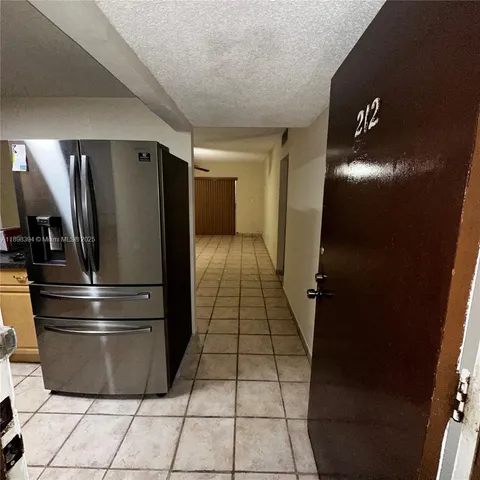 a view of a refrigerator in kitchen and an empty room with wooden floor