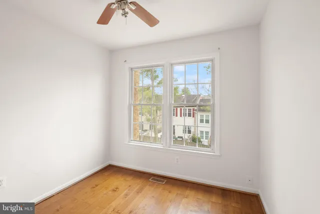 an empty room with wooden floor fan and windows