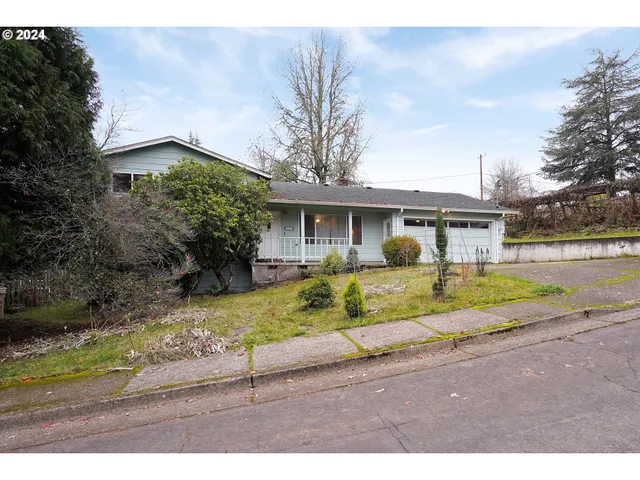 a view of house that has a small yard plants and large trees with wooden fence