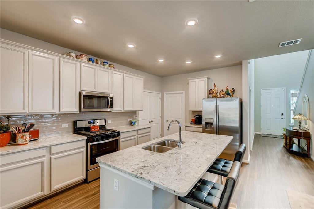 105 Tucana Street Georgetown, TX 78628 - Photo 5 of 17 Kitchen with appliances with stainless steel finishes, a kitchen breakfast bar, light wood-style flooring, white cabinets, and tasteful backsplash