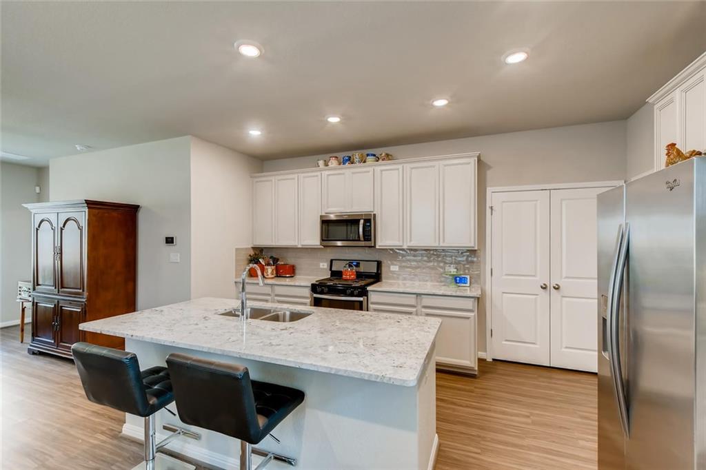 105 Tucana Street Georgetown, TX 78628 - Photo 6 of 17 Kitchen with appliances with stainless steel finishes, a breakfast bar area, light wood finished floors, light stone counters, and an island with sink