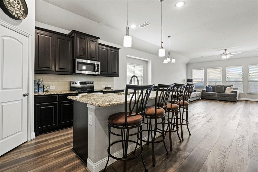 105 Melody Way Red Oak, TX 75154 - Photo 10 of 27 a kitchen with stainless steel appliances granite countertop a stove top oven a refrigerator a sink a dining table and chairs with wooden floor