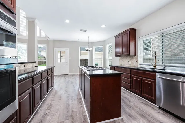 a kitchen with stainless steel appliances granite countertop wooden cabinets a sink dishwasher a stove and a refrigerator