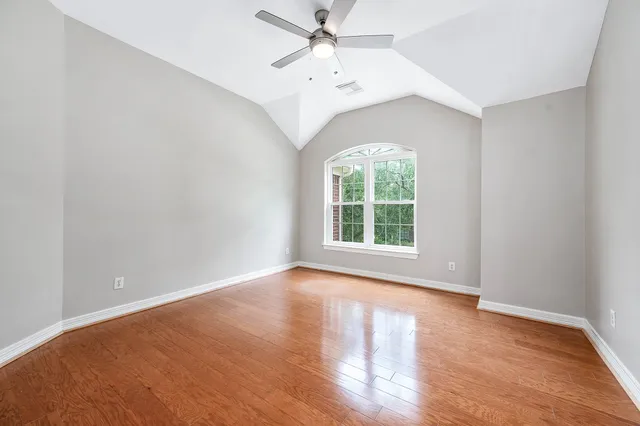 an empty room with wooden floor chandelier fan and windows