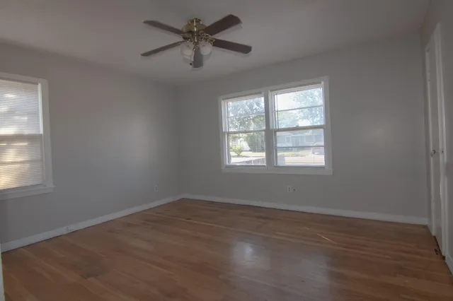 an empty room with wooden floor ceiling fan and windows