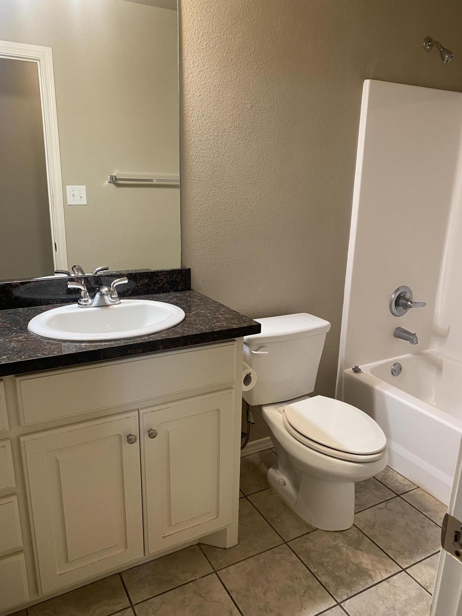 8707 11th Street Lubbock, TX 79416 - Photo 7 of 9 a bathroom with a granite countertop toilet sink and mirror