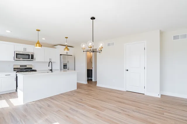 a view of a kitchen with stainless steel appliances granite countertop a refrigerator a stove a microwave and a wooden floor