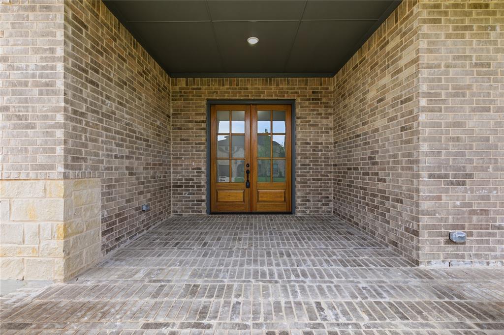 702 Anne Road Van Alstyne, TX 75495 - Photo 2 of 27 Covered entryway featuring a double wood-paneled door with glass inserts, brick-patterned flooring, and a recessed ceiling light fixture