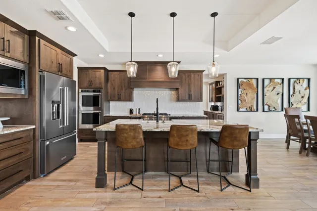 a kitchen with stainless steel appliances kitchen island granite countertop a table chairs and a refrigerator