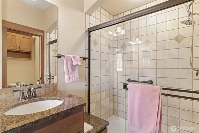 a bathroom with a granite countertop double vanity sink a mirror and a shower