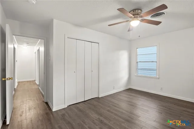 an empty room with wooden floor fan and windows