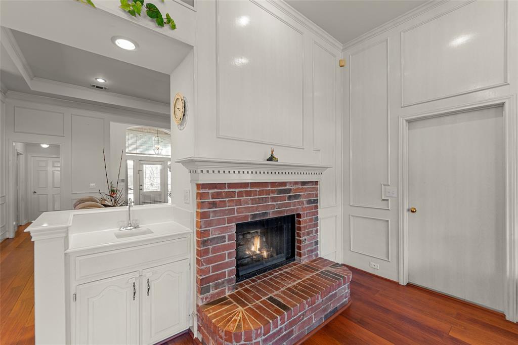 3308 North Spring Drive Richardson, TX 75082 - Photo 9 of 38 The inviting family room features soaring paneled walls, rich wood-like flooring, and a charming brick fireplace that creates a warm focal point. A convenient wet bar adds both functionality and style — perfect for entertaining or everyday enjoyment. Bright and open, this comfortable space is designed for gathering and relaxation.