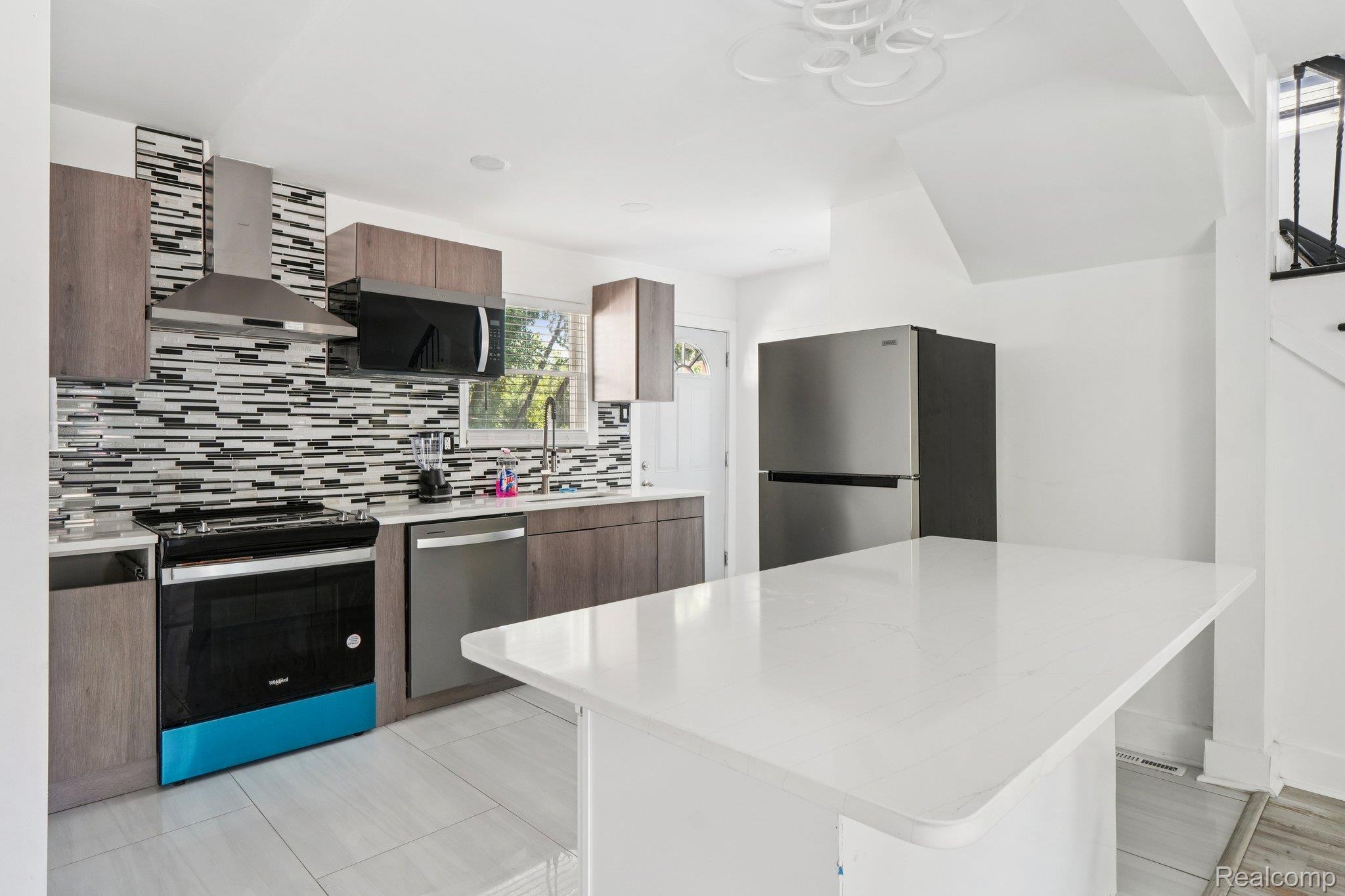 16210 Inverness Street Detroit, MI 48221 - Photo 8 of 29 Contemporary kitchen featuring a white countertop island, stainless steel appliances, wood-finish cabinetry, and a patterned tile backsplash