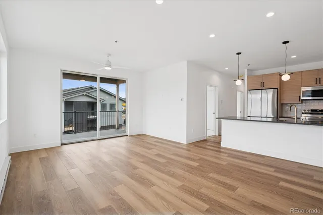 a view of an empty room with wooden floor and a kitchen