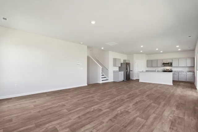 a view of empty room with wooden floor and kitchen