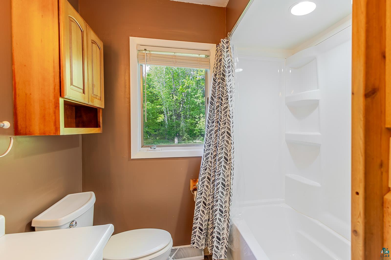 7045 Morris Thomas Road Cloquet, MN 55720 - Photo 15 of 28 Bathroom featuring a white bathtub and shower surround, a single window, built-in wooden cabinetry, and recessed lighting