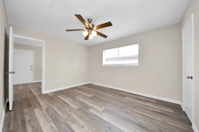 an empty room with wooden floor fan and windows