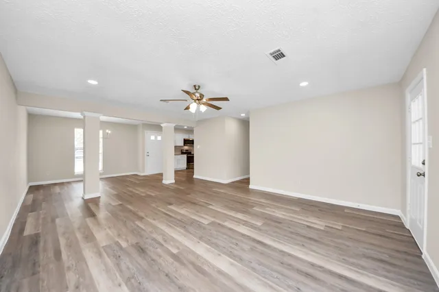 a view of an empty room with wooden floor and a ceiling fan