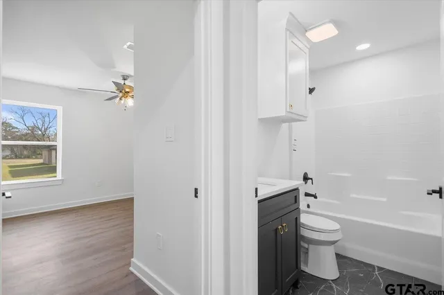 an empty room with wooden floor ceiling fan and windows