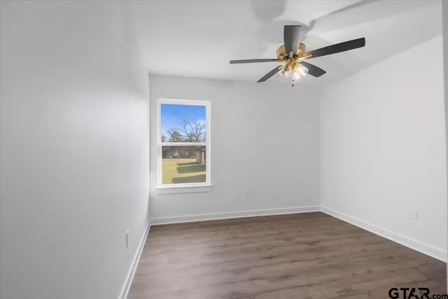 an empty room with wooden floor closet ceiling fan and refrigerator