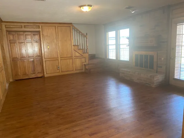 an empty room with wooden floor and windows with curtains