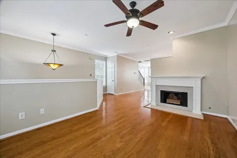 an empty room with wooden floor a ceiling fan a fireplace and windows