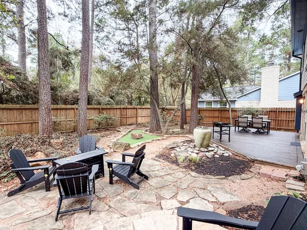 a view of a patio with a dining table and chairs with wooden fence and large trees
