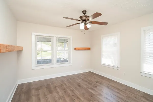 an empty room with wooden floor fan and windows