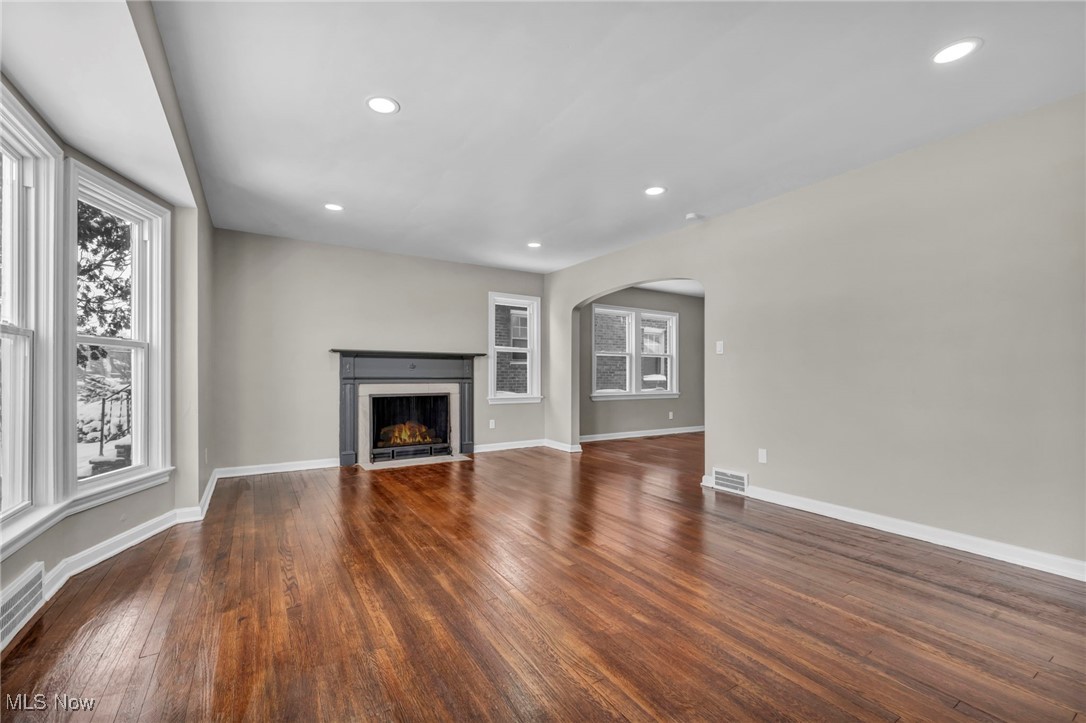 13614 Cedar Road Cleveland, OH 44118 - Photo 5 of 46 Unfurnished living room featuring arched walkways, a fireplace with flush hearth, visible vents, baseboards, and dark wood finished floors