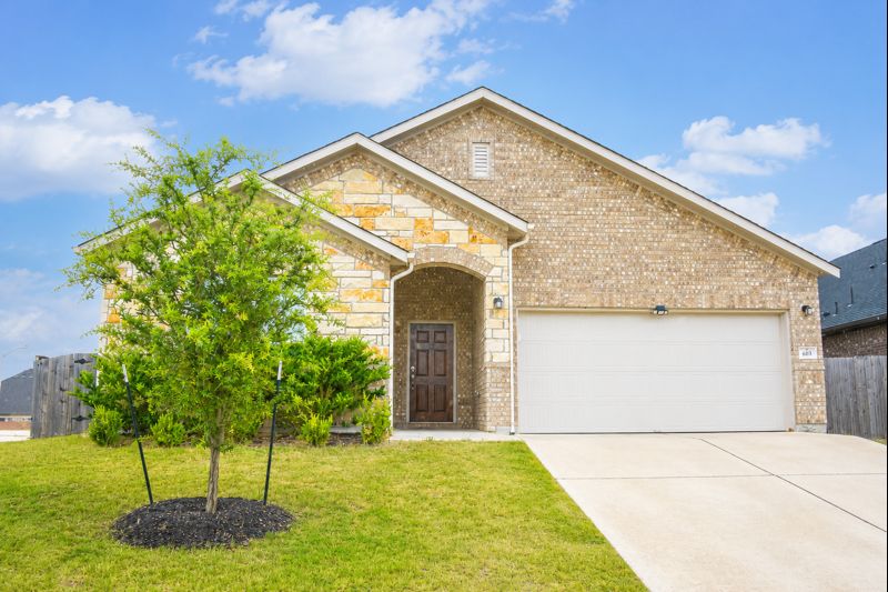 693 Durian Loop Buda, TX 78610 - Photo 1 of 27 A striking exterior combines brick and stone, showcasing an attached garage and a welcoming covered entry.