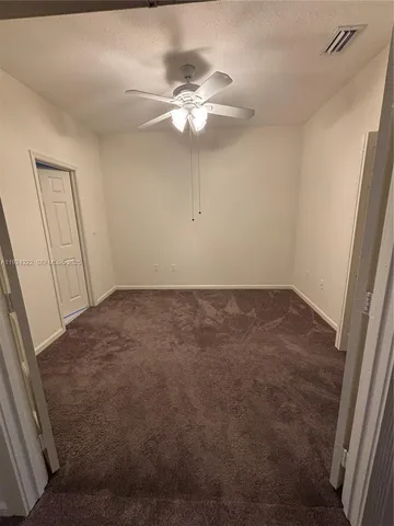 an empty room with a chandelier fan and wooden floor