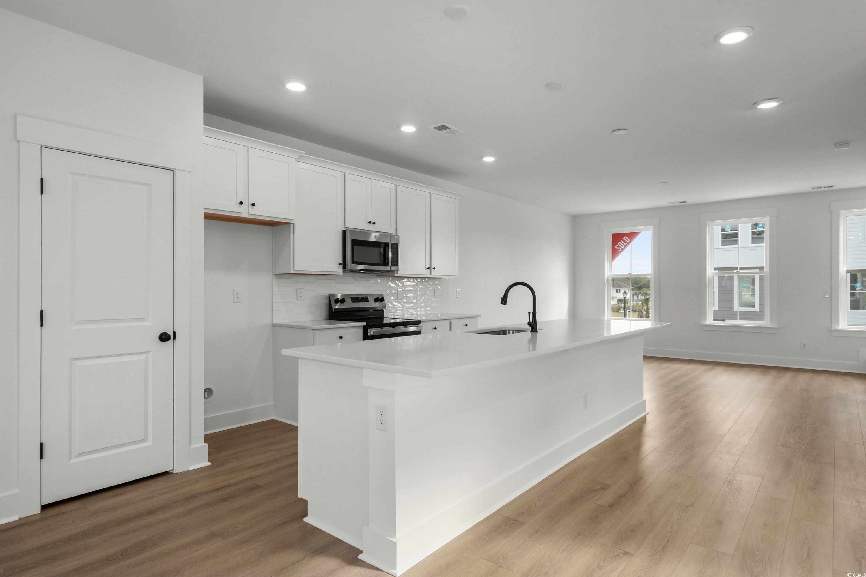 4414 Kingsport Road, Unit 1402 Little River, SC 29566 - Photo 7 of 34 Kitchen featuring white cabinets, stainless steel appliances, a center island with sink, decorative backsplash, and dark wood-type flooring