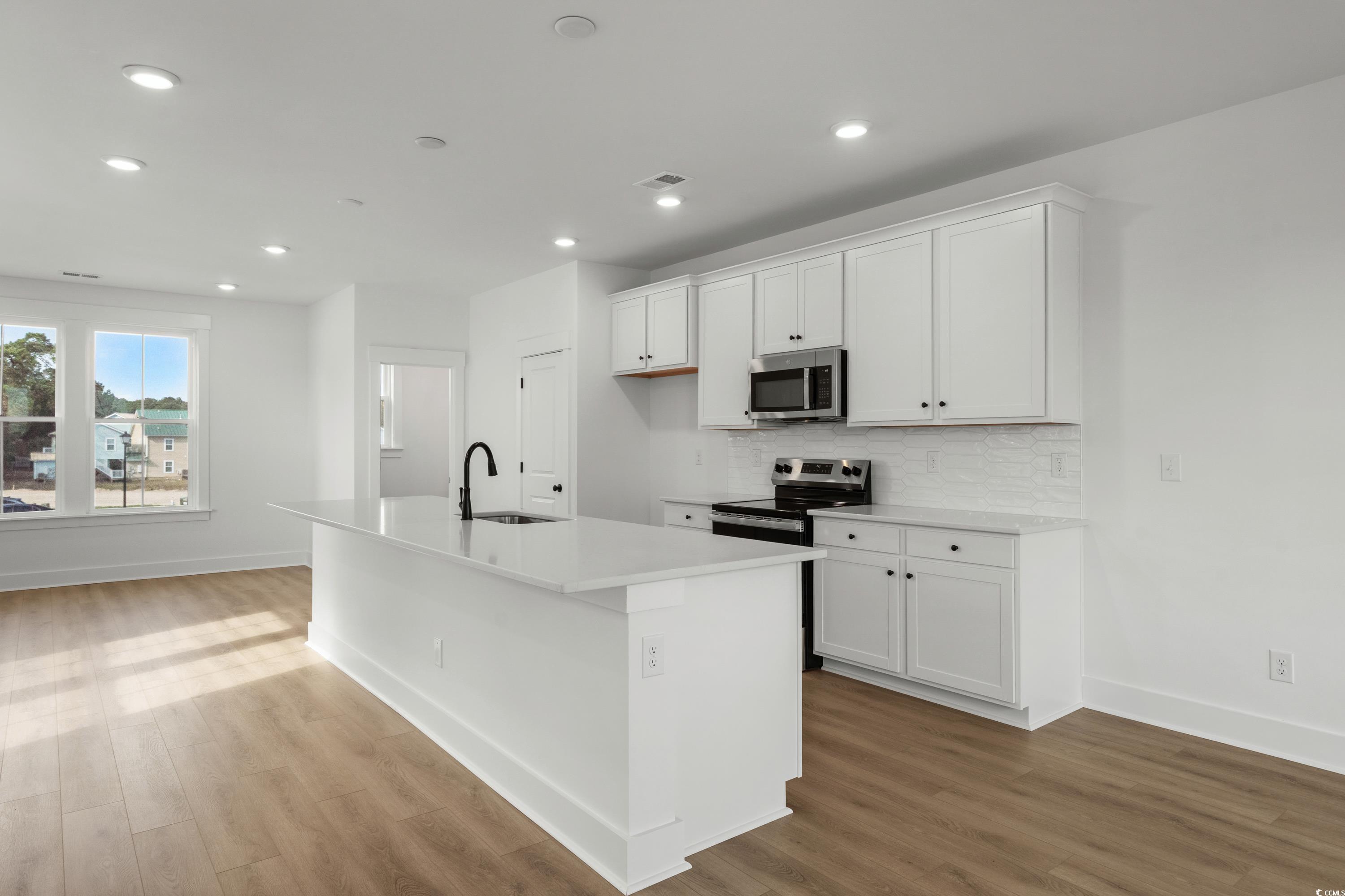 4414 Kingsport Road, Unit 1402 Little River, SC 29566 - Photo 8 of 34 Kitchen with stainless steel appliances, white cabinets, a kitchen island with sink, light wood finished floors, and decorative backsplash
