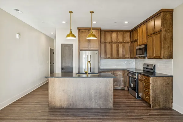 a kitchen with stainless steel appliances granite countertop a sink a stove a refrigerator cabinets and wooden floor