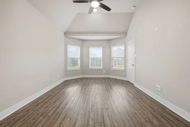 an empty room with wooden floor chandelier fan and windows