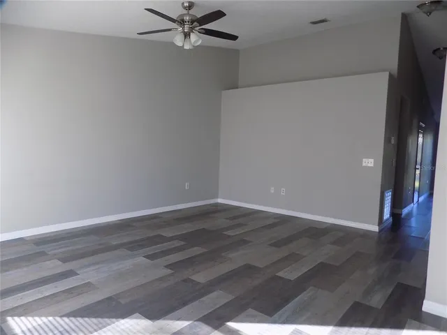 an empty room with wooden floor fan and windows