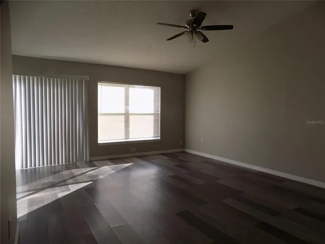an empty room with wooden floor fan and windows