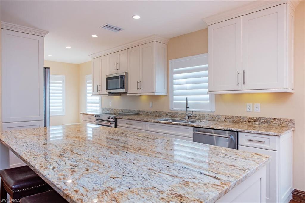 Kitchen featuring white cabinetry, light stone counters, stainless steel appliances, a breakfast bar, and a kitchen island