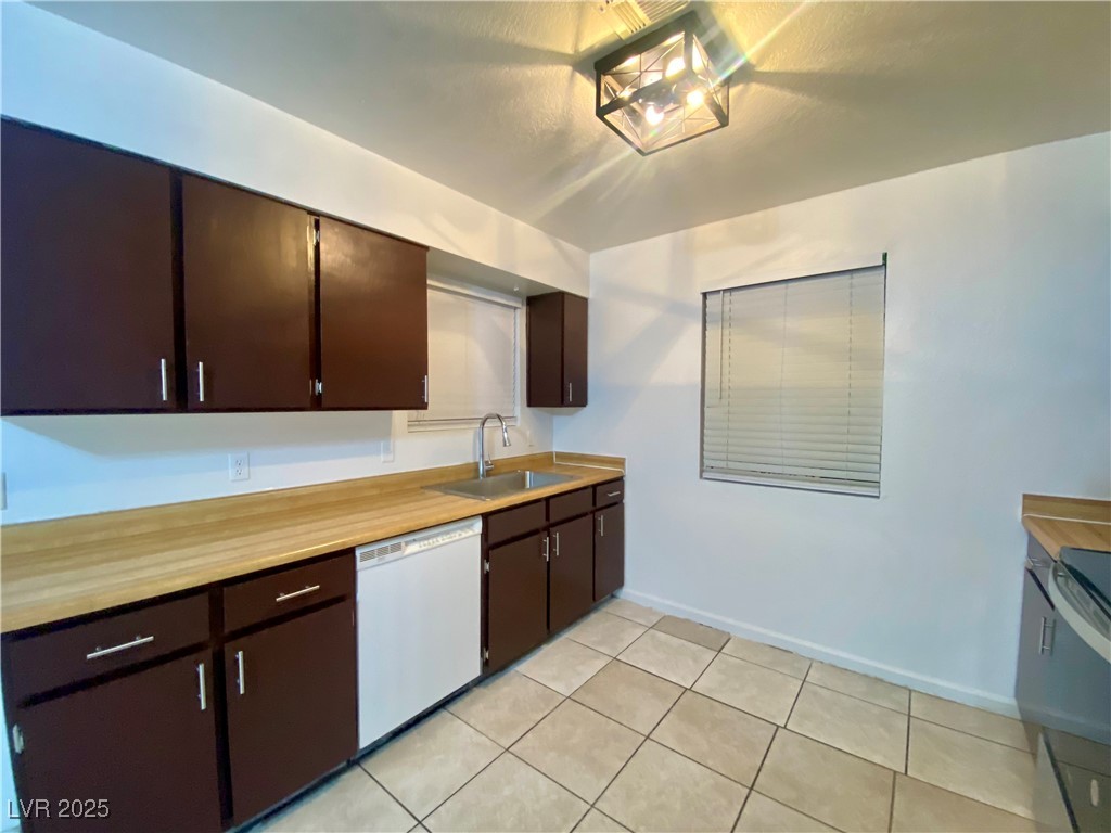5284 Hagemann Lane, Unit D Las Vegas, NV 89110 - Photo 5 of 30 Kitchen featuring dark brown cabinetry, white dishwasher, light countertops, light tile patterned flooring, and stainless steel range
