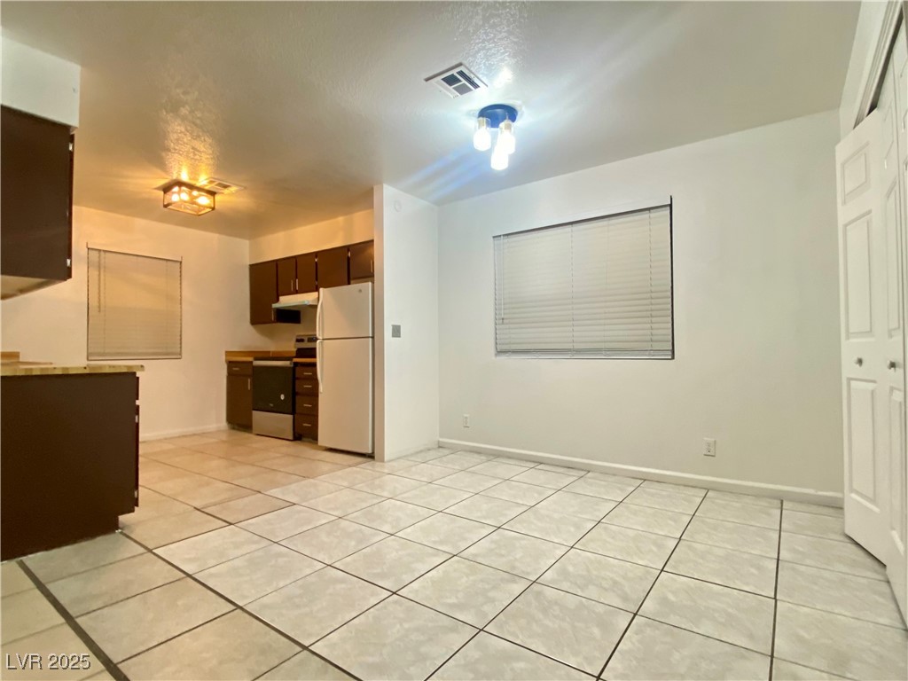5284 Hagemann Lane, Unit D Las Vegas, NV 89110 - Photo 7 of 30 Kitchen featuring freestanding refrigerator, stainless steel range with electric cooktop, light countertops, dark brown cabinetry, and light tile patterned floors