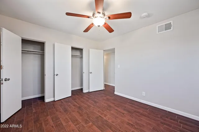 an empty room with wooden floor ceiling fan and windows