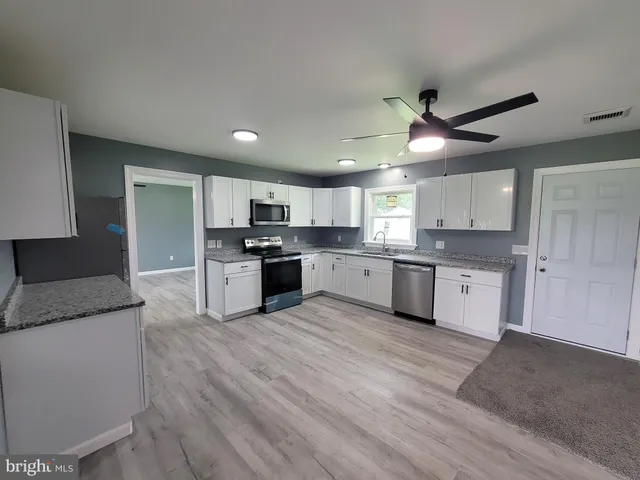 a large kitchen with granite countertop a stove top oven a sink dishwasher a refrigerator and white cabinets with wooden floor