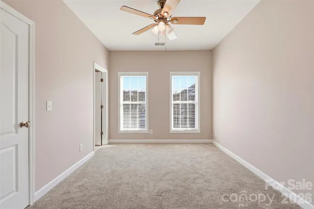 an empty room with chandelier fan and windows
