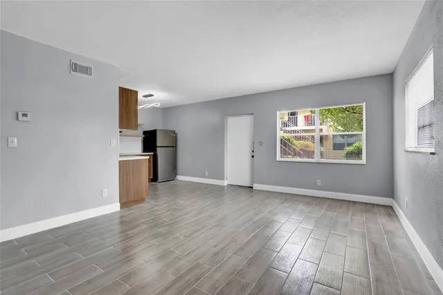 an empty room with wooden floor kitchen view and windows