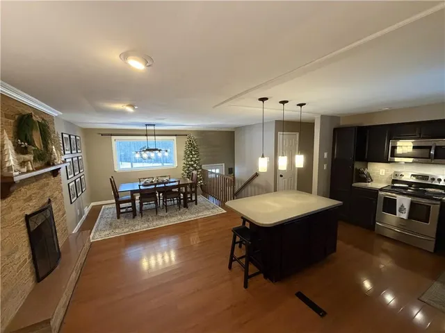 a kitchen with stainless steel appliances kitchen island granite countertop a refrigerator a stove and a dining table with wooden floor