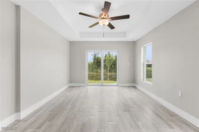 an empty room with wooden floor chandelier fan and windows
