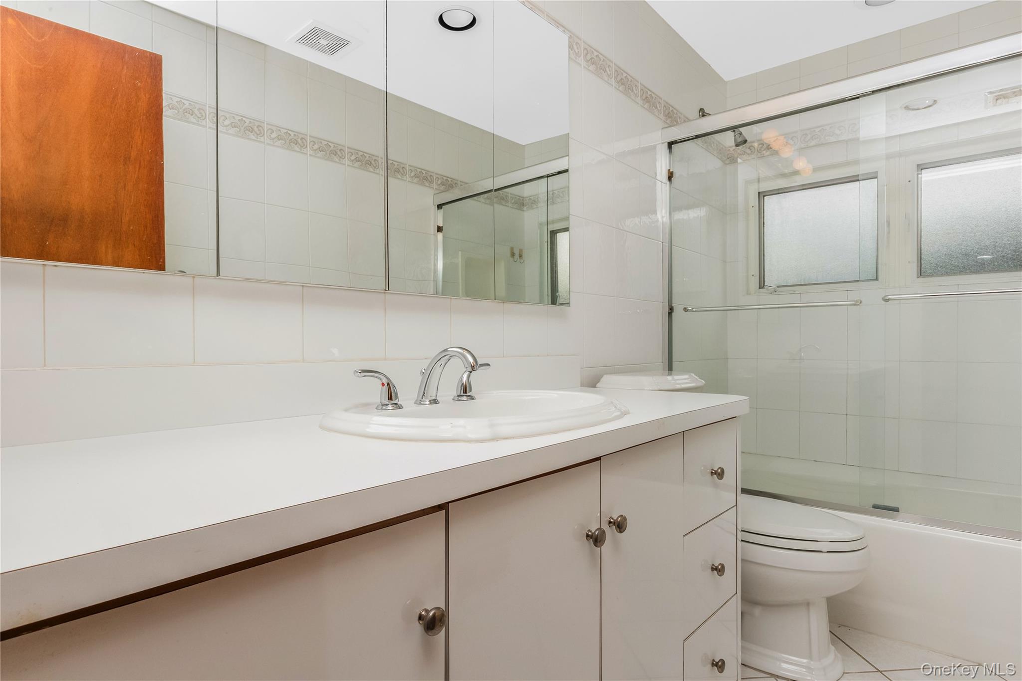 29 Randy Lane Plainview, NY 11803 - Photo 24 of 38 Hall Bath. White vanity integrated sink, chrome faucet, mirrored medicine cabinet, built-in bathtub with glass enclosure, and white tiled walls