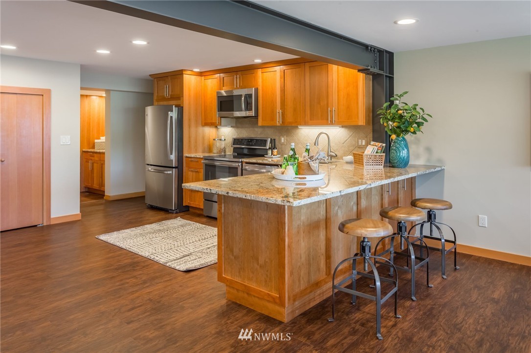 3500 West Commodore Way Seattle, WA 98199 - Photo 19 of 25 a kitchen with stainless steel appliances granite countertop a stove a refrigerator a sink a dining table and chairs with wooden floor